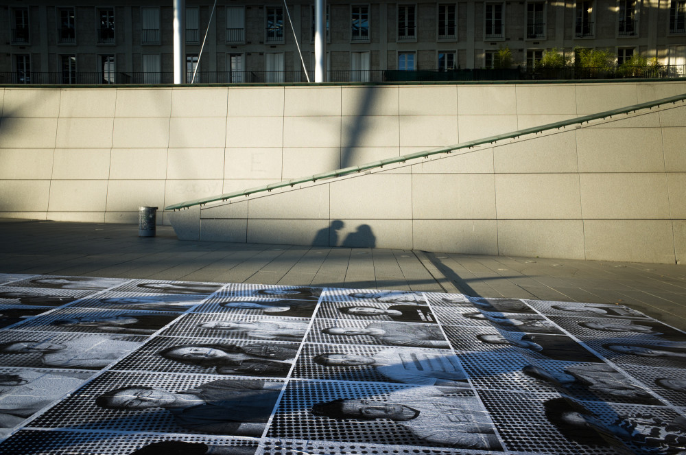 Deux ombres s'attardent près des photos du projet inside out, devant la gare d'Amiens.